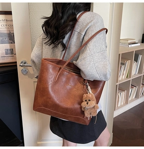 Detalle del bolso tote marrón oscuro con colgante de perro de peluche y logo dorado