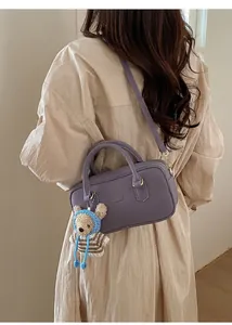 Détail d'un sac bandoulière en cuir violet avec charm ours et accessoires dorés