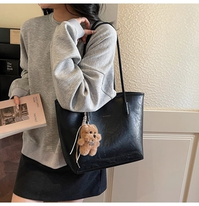 Detalle de bolso tote de cuero negro con un colgante de oso de peluche marrón y logo dorado