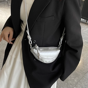 Mini silver saddle bag with metallic finish and thick rope shoulder strap worn by model