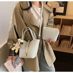 Detail view of light blue bucket bag with gold lock, plush charm, and pebbled leather texture