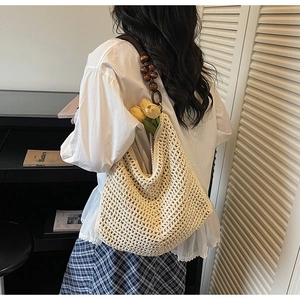 Detail of hollow knit tote bag featuring dark brown wooden beads on a white woven strap