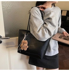 Detalle del bolso tote de cuero negro con textura de grano y colgante de osito de peluche