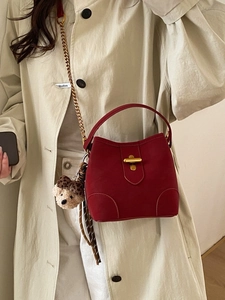 Sac seau rouge foncé avec chaîne dorée et breloque ours léopard sur un manteau beige