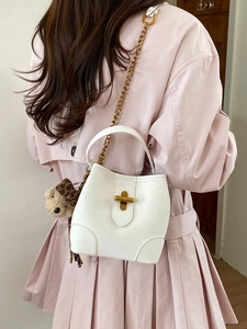 Sac seau blanc avec chaîne dorée et charm ours porté sur un trench-coat rose