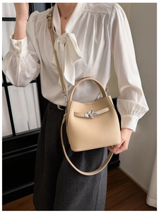 Detail of beige lychee pattern leather bucket bag with metallic twist lock and handle