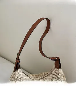 Detail view of beige woven straw bag with adjustable brown leather shoulder strap and metal buckle
