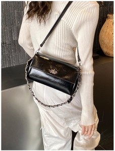 Chic black glossy shoulder bag with silver chain strap shown on a model outfit
