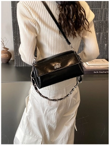 Detail view of black patent leather crossbody bag with chain and twist lock on a model