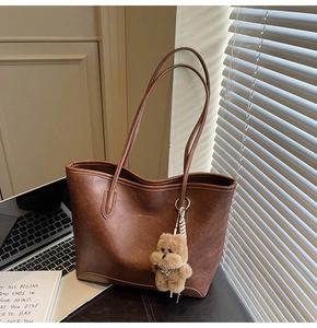 Detalle del bolso tote de cuero marrón vintage con colgante de oso y correa larga al hombro