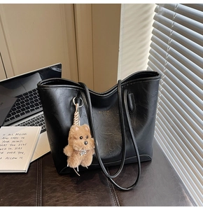 Primer plano de bolso tote de cuero negro con logo dorado y colgante de oso de peluche