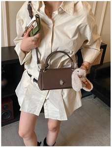 Brown lychee grain leather crossbody bag with a twist handle and a grey plush bunny charm
