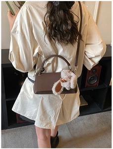Detail view of dark brown pebbled leather handbag with cute plush bunny charm on shoulder