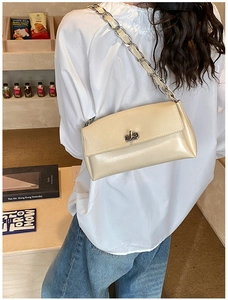Detail of a beige glossy shoulder bag with silver twist lock and chain strap on a model