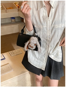 Detail of black pebbled leather handbag with a fluffy rabbit charm and metal clasp