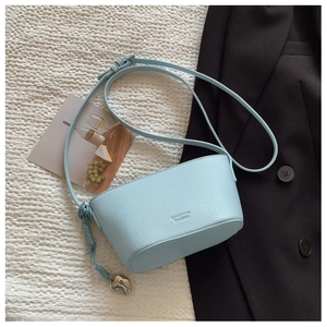 Detail of light blue lychee grain leather crossbody bag with heart pendant and knot strap