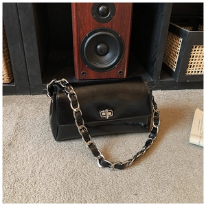 Close-up of black glossy leather bag featuring silver twist-lock and chain strap detail