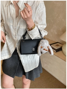 Close-up of black litchi grain leather handbag with silver lock and plush bunny charm