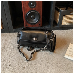 Detail of black glossy shoulder bag with silver turn-lock and metal chain strap