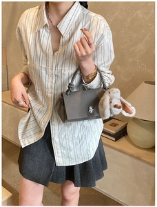 Detail of dark grey leather handbag with silver twist lock and beige bunny charm accessory