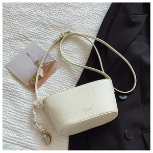 Detailed macro view of cream-colored litchi grain leather bag with heart metal pendant