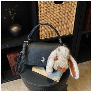 Detailed shot of black litchi leather handbag with silver lock and plush bunny charm