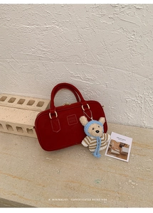 Nahaufnahme der roten Boston-Handtasche mit Logoprägung und süßem Bären-Anhänger
