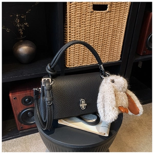 Detail of black lychee leather handbag with silver lock and plush bunny charm accessory