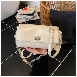 Detail view of a cream leather handbag with silver metal lock and chain handle