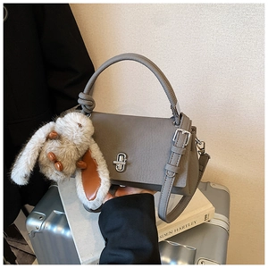 Detail view of the gray lychee pattern leather handbag with silver lock and plush bunny charm