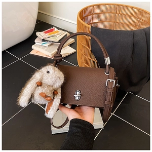 Detail view of coffee leather handbag featuring silver lock and cute plush bunny charm