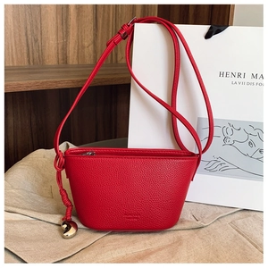 Close-up of red litchi grain leather bag with a gold heart pendant on beige linen cloth