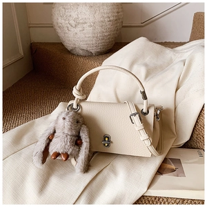 Detail of off-white lychee grain leather handbag with silver clasp and plush rabbit charm