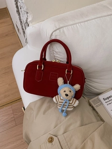 Minimalistische rote Handtasche mit Bärenanhänger und goldenen Details auf einem Sofa