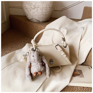 Detail view of cream lychee texture leather bag with metal lock and plush bunny charm