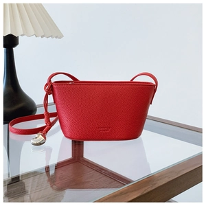 Detail of red pebbled leather handbag with silver heart pendant on a wooden table