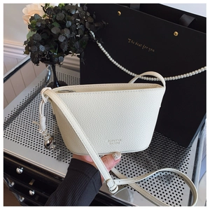 Detailed shot of beige lychee leather bag with knot strap and silver metal charms