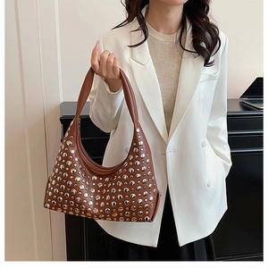 Braune Hobo-Bag aus Leder mit silbernen Nieten, getragen von Model im weißen Blazer