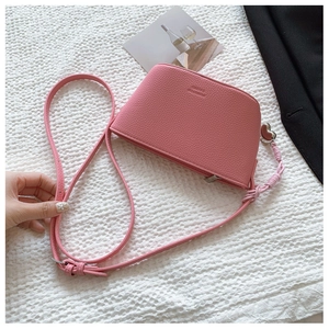 Close-up of pink crossbody bag with litchi grain texture and a heart-shaped metal charm