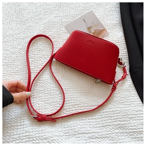 Detail of red lychee textured leather crossbody bag with silver heart charm and strap