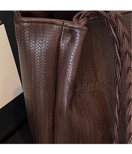 Detail shot of the hand-woven texture and handle on a dark brown faux leather tote bag