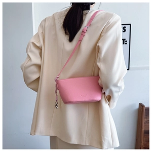 Rear view of a pink lychee leather crossbody bag styled with a cream blazer and woven knot charm