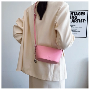 Detail of pink lychee leather crossbody bag with heart pendant worn by model