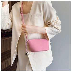 Detail view of pink lychee leather crossbody bag with silver bean charm and knot strap
