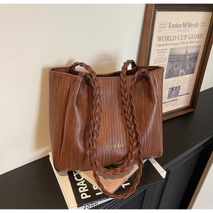 Close-up of brown woven leather tote bag with thick braided handles and embossed text
