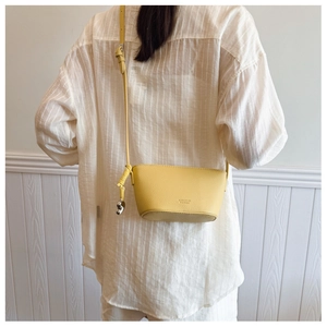 Detail of bright yellow lychee leather bucket bag with silver charm on adjustable strap