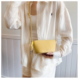Detail of lemon yellow leather crossbody bag with silver bear pendant on white wood backdrop