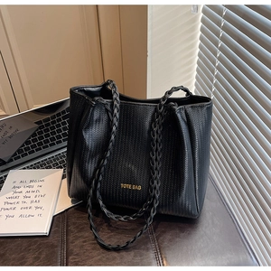 Detail of black woven texture tote bag with rope handles and golden text on an office desk