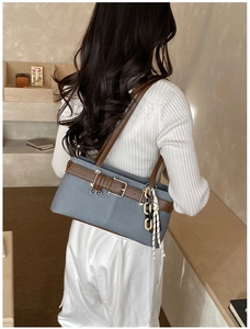 Détail du sac bandoulière en denim bleu avec lanières en cuir brun et chaîne beige