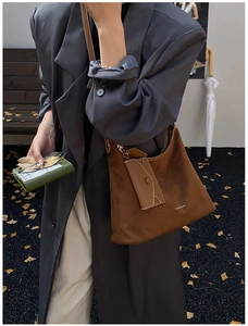 Close-up of brown suede tote bag featuring a matching envelope charm in an urban setting